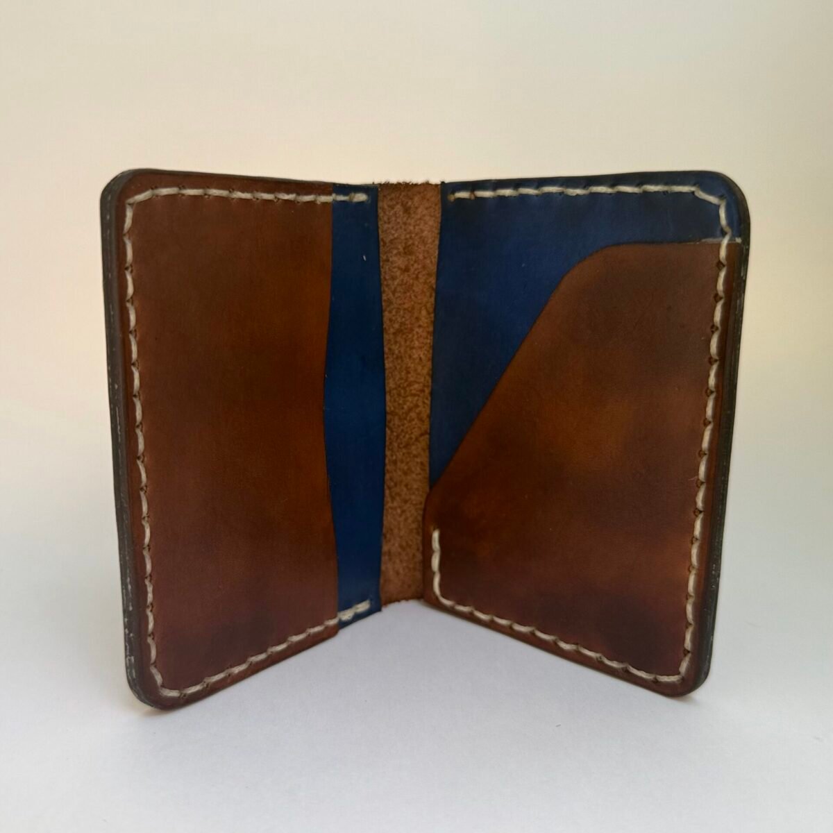 Handmade leather wallet open to show brown and navy interior with cream stitching