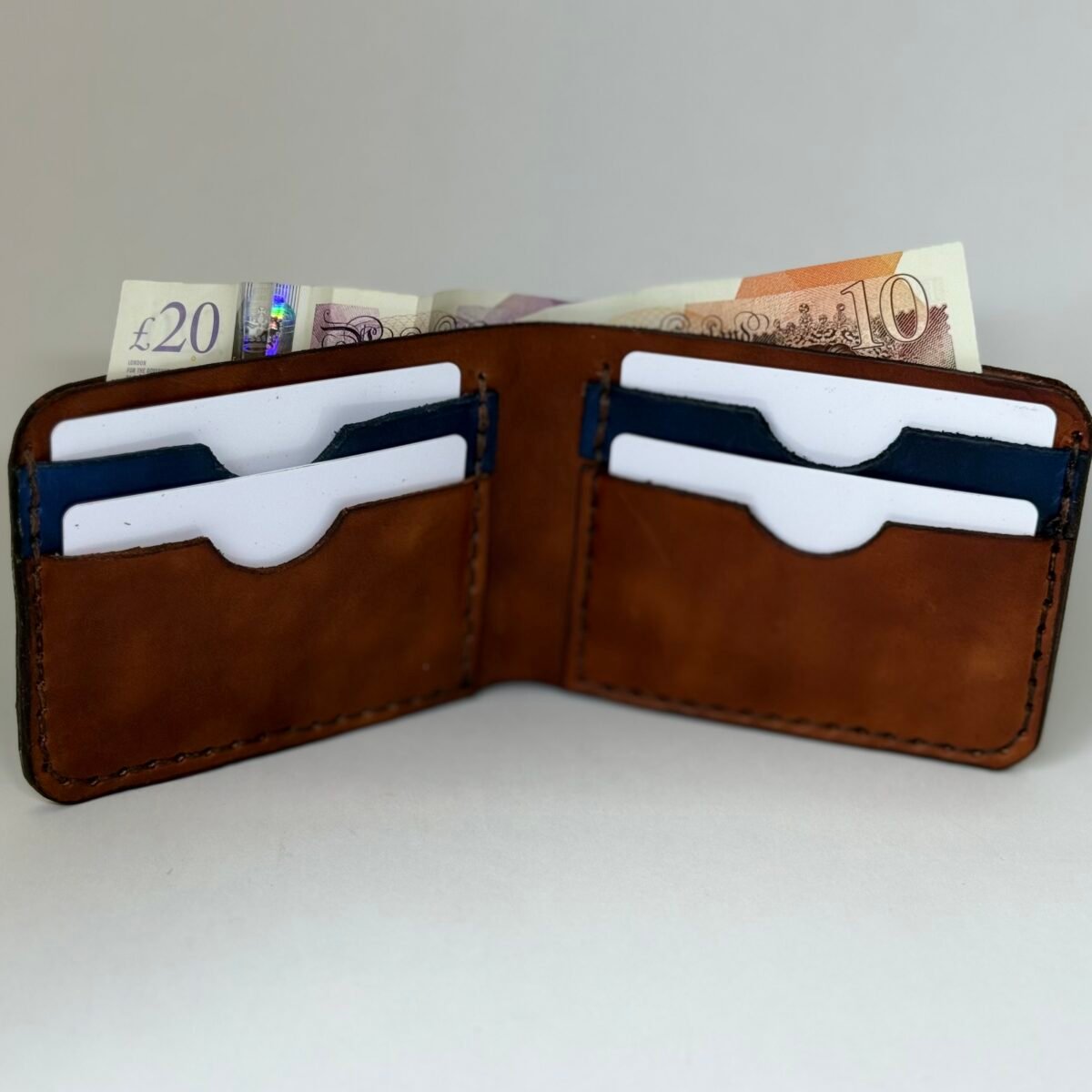 Handmade leather bi-fold wallet shown open with cards and UK banknotes in the slots